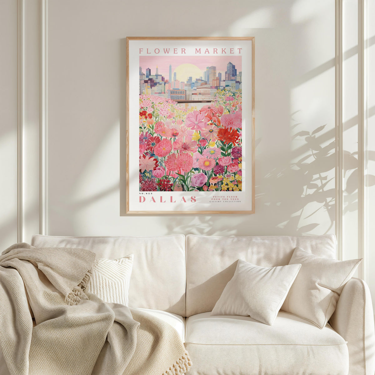 a framed poster of a cityscape with a field of flowers in the foreground, hanging on a wall above a white couch.