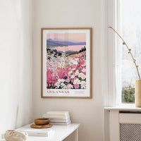 a framed poster of a scenic landscape with mountains and flowers hanging on a wall in a room.