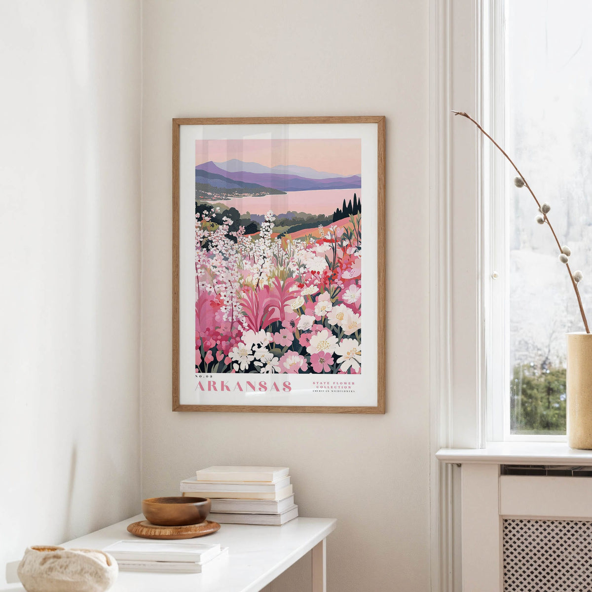 a framed poster of a scenic landscape with mountains and flowers hanging on a wall in a room.
