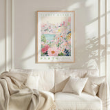 a framed poster of a cityscape with a floral scene, hanging on a wall above a white couch with a blanket draped over it.