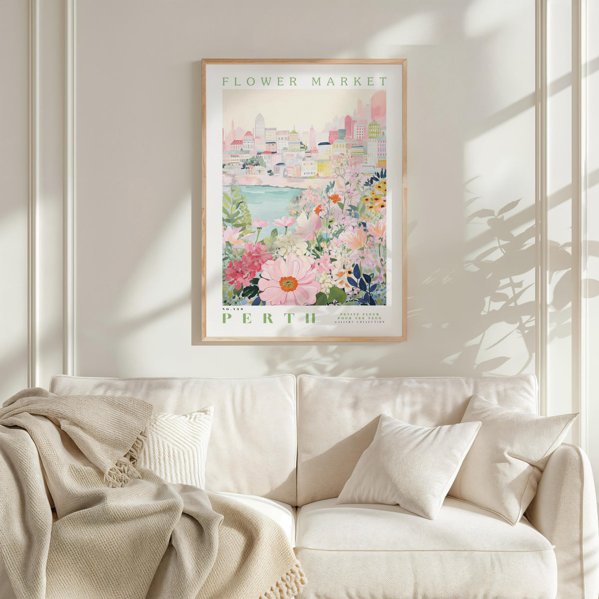 a framed poster of a cityscape with a floral scene, hanging on a wall above a white couch with a blanket draped over it.