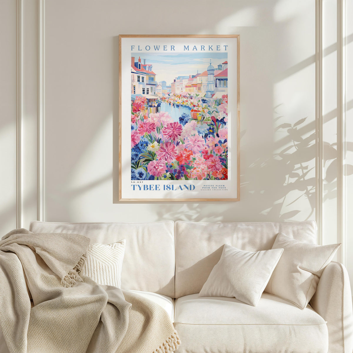 a framed poster of a colorful floral scene hanging on a wall above a white couch with a blanket draped over it.