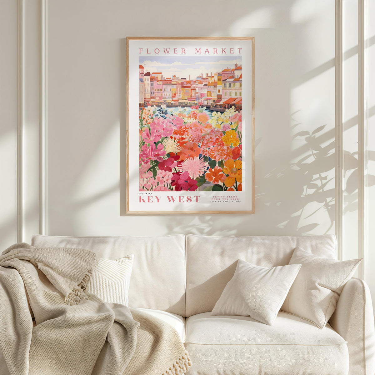 a framed poster of a colorful floral scene hanging on a wall above a white couch with a blanket draped over it.