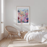a bedroom with a bed, a woven chair, and a framed poster of a colorful floral scene hanging on the wall.