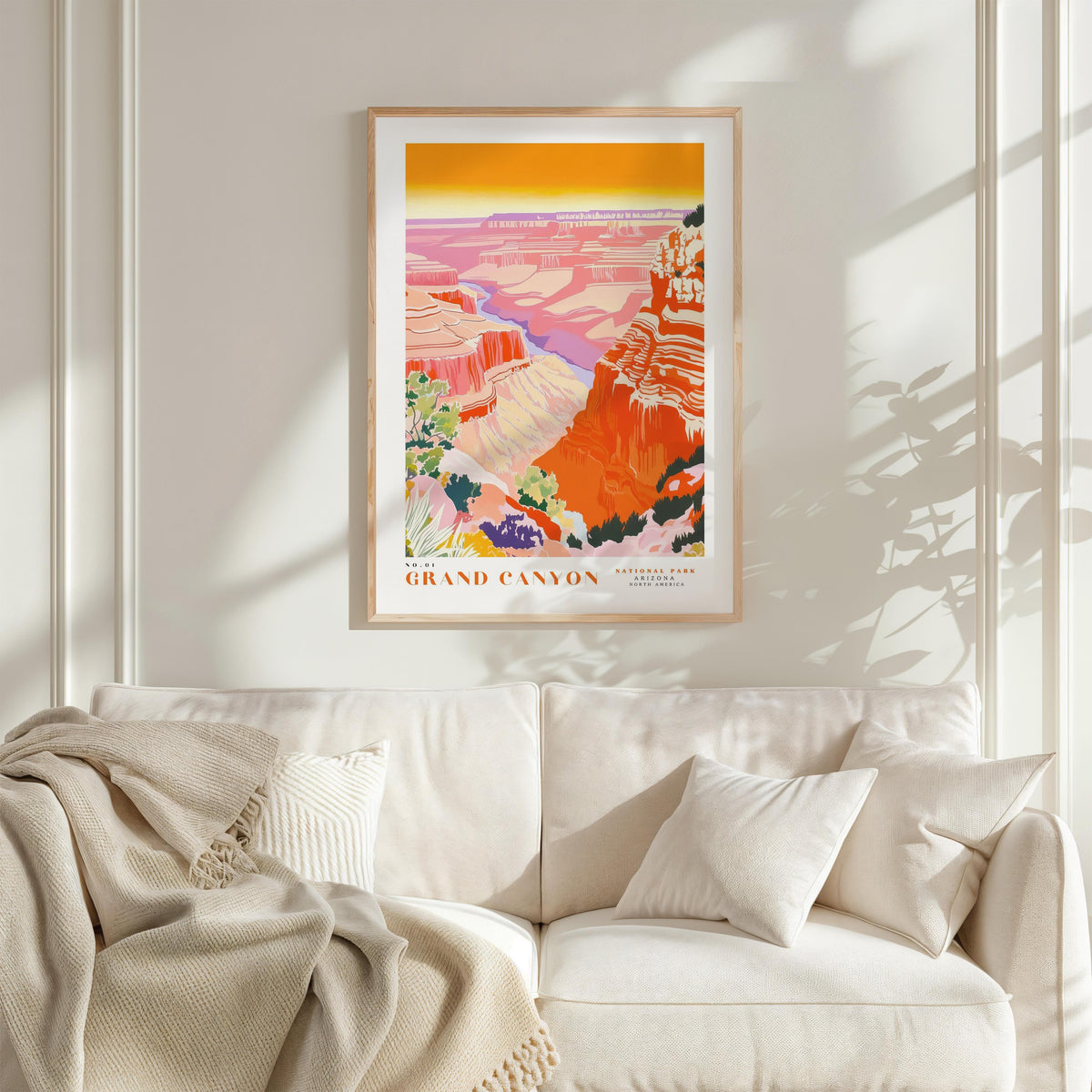 a framed poster of the Grand Canyon hanging on a wall above a white couch with a blanket draped over it.