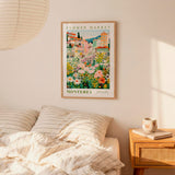 a bedroom setting with a framed poster of a flower market hanging on the wall above a bed with striped bedding.