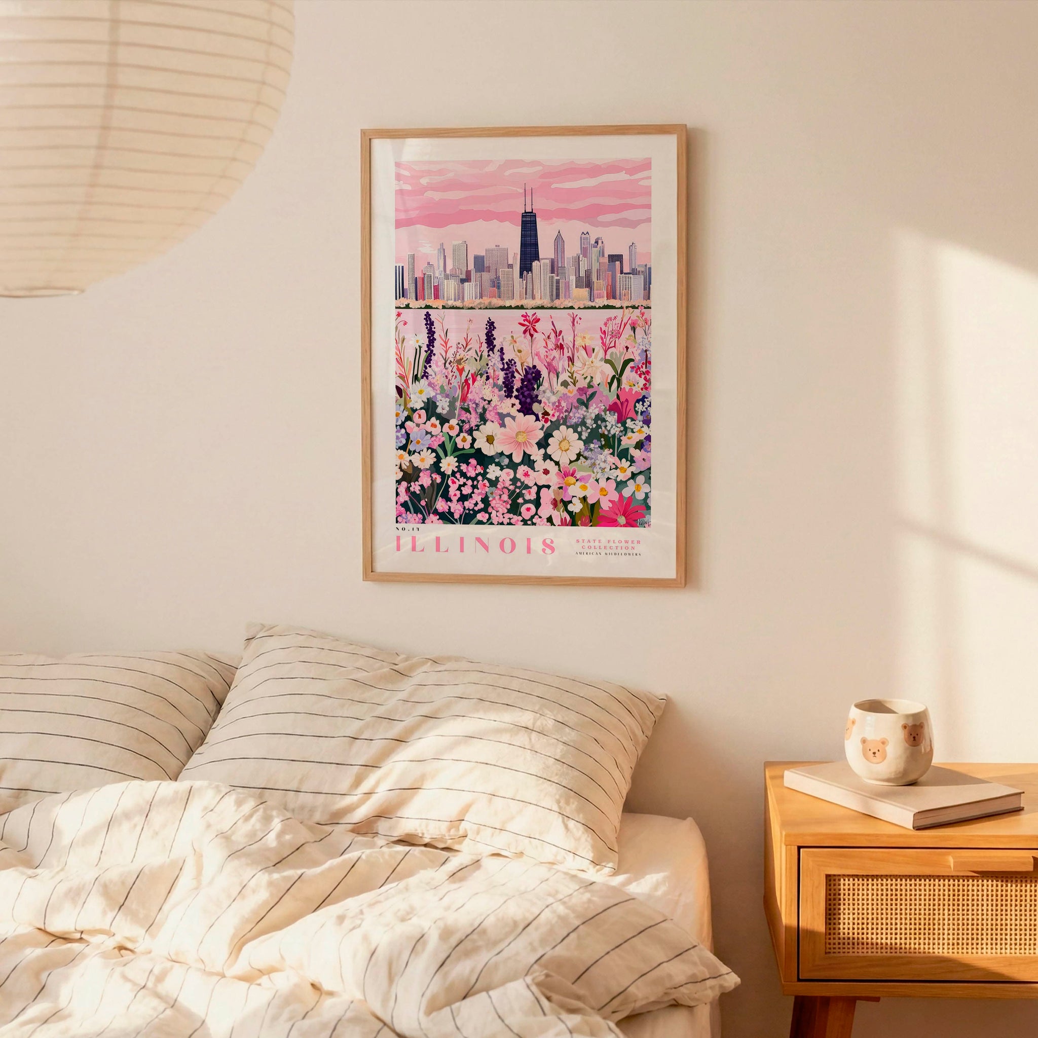 a bedroom setting with a framed poster of a city skyline and a bed with striped pillows. There is also a nightstand with a coffee mug and a book on it.