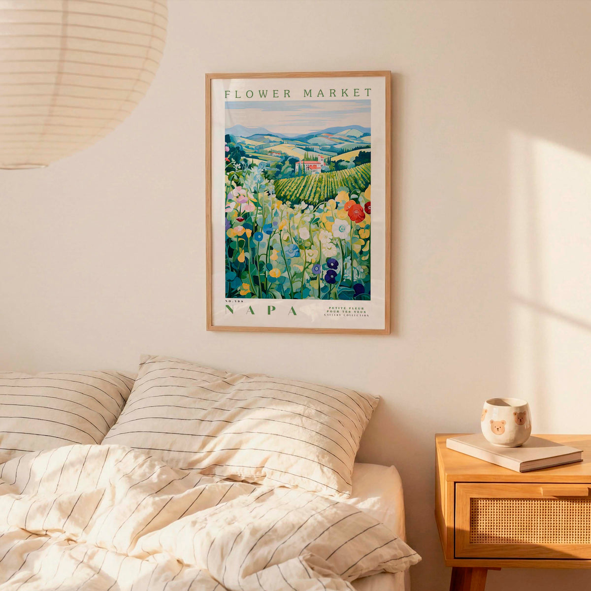 a bedroom setting with a framed poster of a flower market in Napa, California, hanging on the wall above a bed with striped pillows.