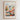 The image is a framed poster depicting a woman standing amidst a colorful garden filled with various flowers.