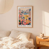 a bedroom setting with a framed poster of a flower market in New York hanging on the wall above a bed with striped pillows.