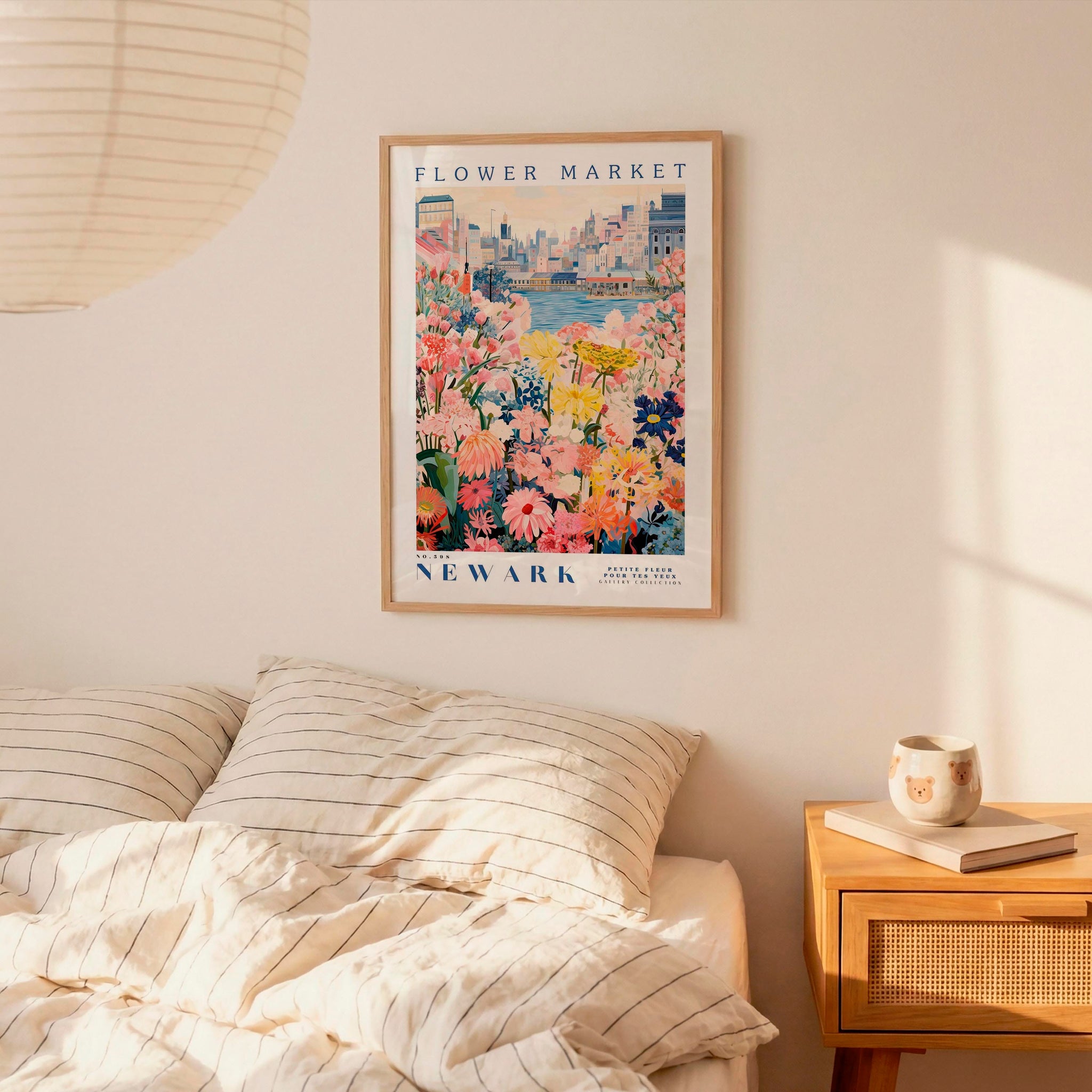a bedroom setting with a framed poster of a flower market in New York hanging on the wall above a bed with striped pillows.