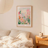 a bedroom with a framed poster of a flower market in Miami hanging on the wall above a bed with striped pillows.
