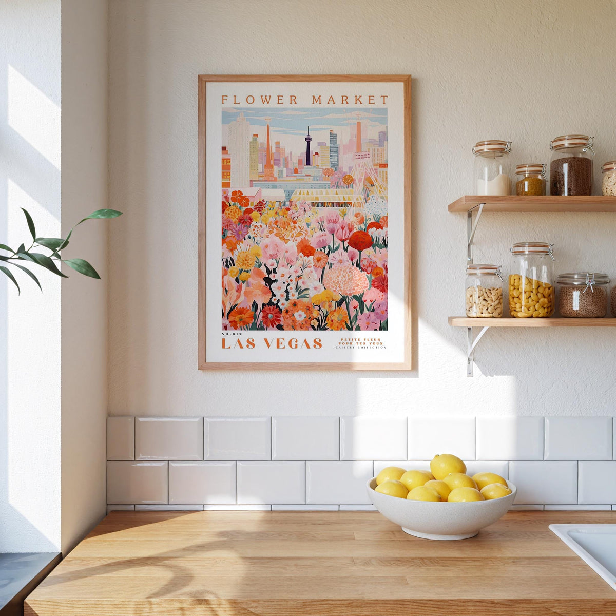 a framed poster of a colorful cityscape with a flower market in the background, hanging on a wall above a wooden counter with a bowl of lemons.