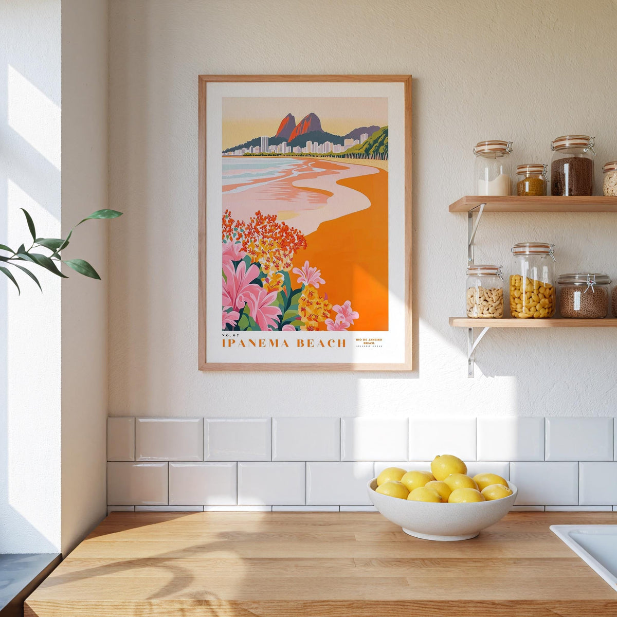 a kitchen counter with a bowl of lemons, a framed poster of Ipanema Beach, and a shelf with jars and containers.
