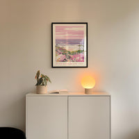 a white cabinet with a plant and a lamp on top, and a framed picture hanging on the wall above it.