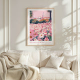 a framed poster of a field of flowers with a pink and green background, hanging on a white wall above a white couch with a blanket draped over it.