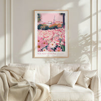 a framed poster of a field of flowers with a pink and green background, hanging on a white wall above a white couch with a blanket draped over it.