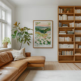 a cozy living room with a large window, a comfortable leather sofa, a wooden bookshelf filled with books, and a framed poster of a flowery landscape hanging on the wall.