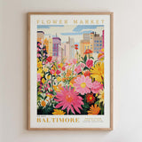 The image is a framed poster depicting a vibrant and colorful flower market in Baltimore, with a variety of flowers and plants in the foreground and a cityscape in the background.