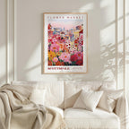 a poster of a colorful flower market displayed on a wall above a white couch with a blanket draped over it.