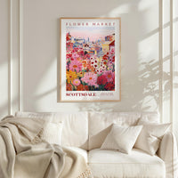a poster of a colorful flower market displayed on a wall above a white couch with a blanket draped over it.