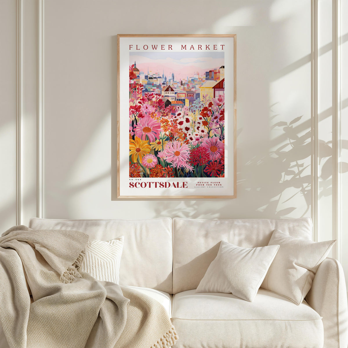 a poster of a colorful flower market displayed on a wall above a white couch with a blanket draped over it.
