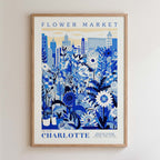 The image is a framed poster depicting a cityscape with a variety of flowers and plants in the foreground, and buildings in the background.
