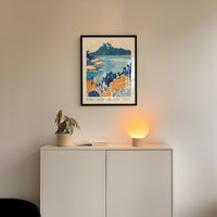a white cabinet with a plant and a lamp on top, and a framed poster of a tropical beach scene hanging on the wall above it.