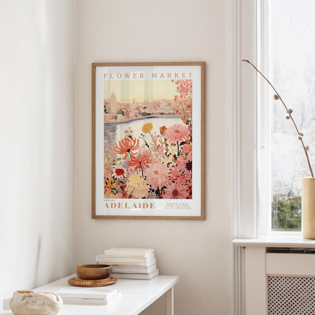 a framed poster of a cityscape with a floral design, hanging on a wall in a room with a white table and a window.