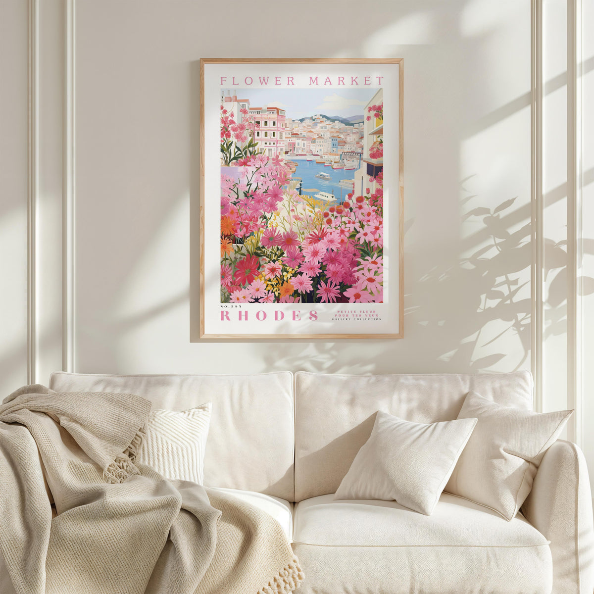 a framed poster of a flower market in Rhodes, Greece, hanging on a wall above a white couch with a blanket draped over it.