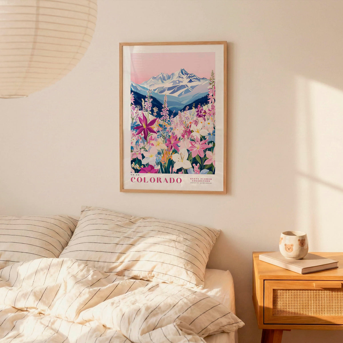 a bedroom scene with a framed poster of a mountain landscape hanging on the wall above a bed with striped pillows.