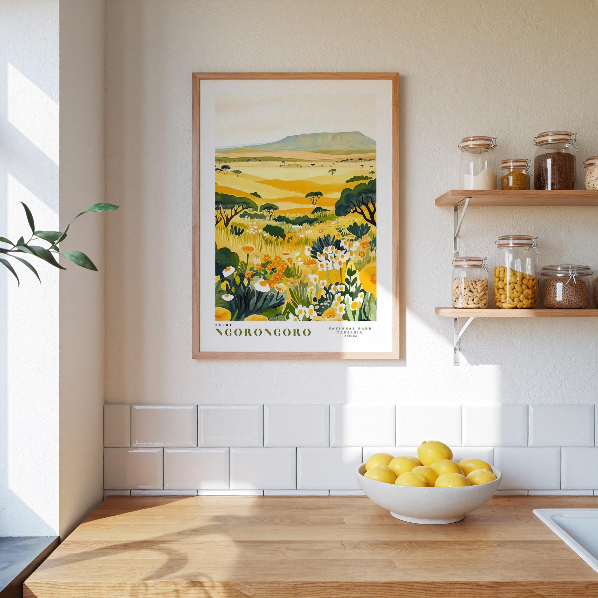 a kitchen counter with a bowl of lemons, a framed print of a landscape, and shelves with jars and containers.