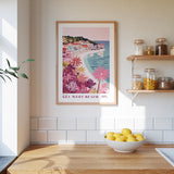 a framed poster of a tropical beach scene with a small town, hanging on a wall above a kitchen counter with a bowl of lemons and jars of food.