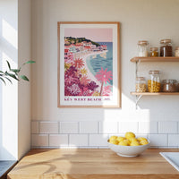 a framed poster of a tropical beach scene with a small town, hanging on a wall above a kitchen counter with a bowl of lemons and jars of food.