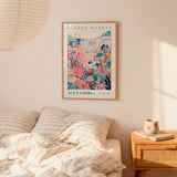 a bedroom scene with a framed poster of a colorful floral scene hanging on the wall above a bed with striped pillows.