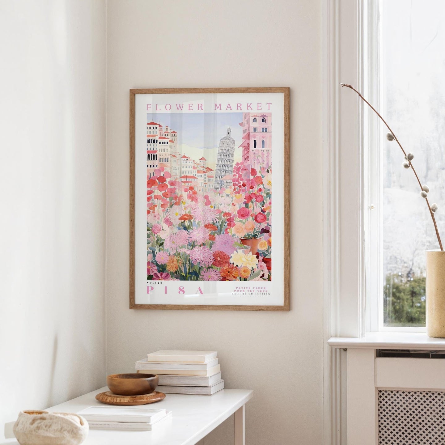 a framed poster of a colorful floral scene hanging on a wall, with a white table and a vase of flowers nearby.