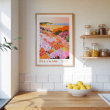 a framed poster of a colorful garden scene hanging on a wall above a wooden countertop with a bowl of lemons.