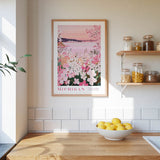 a kitchen scene with a framed poster of a flowery landscape hanging on the wall, a bowl of lemons on the counter, and shelves displaying various jars and containers.