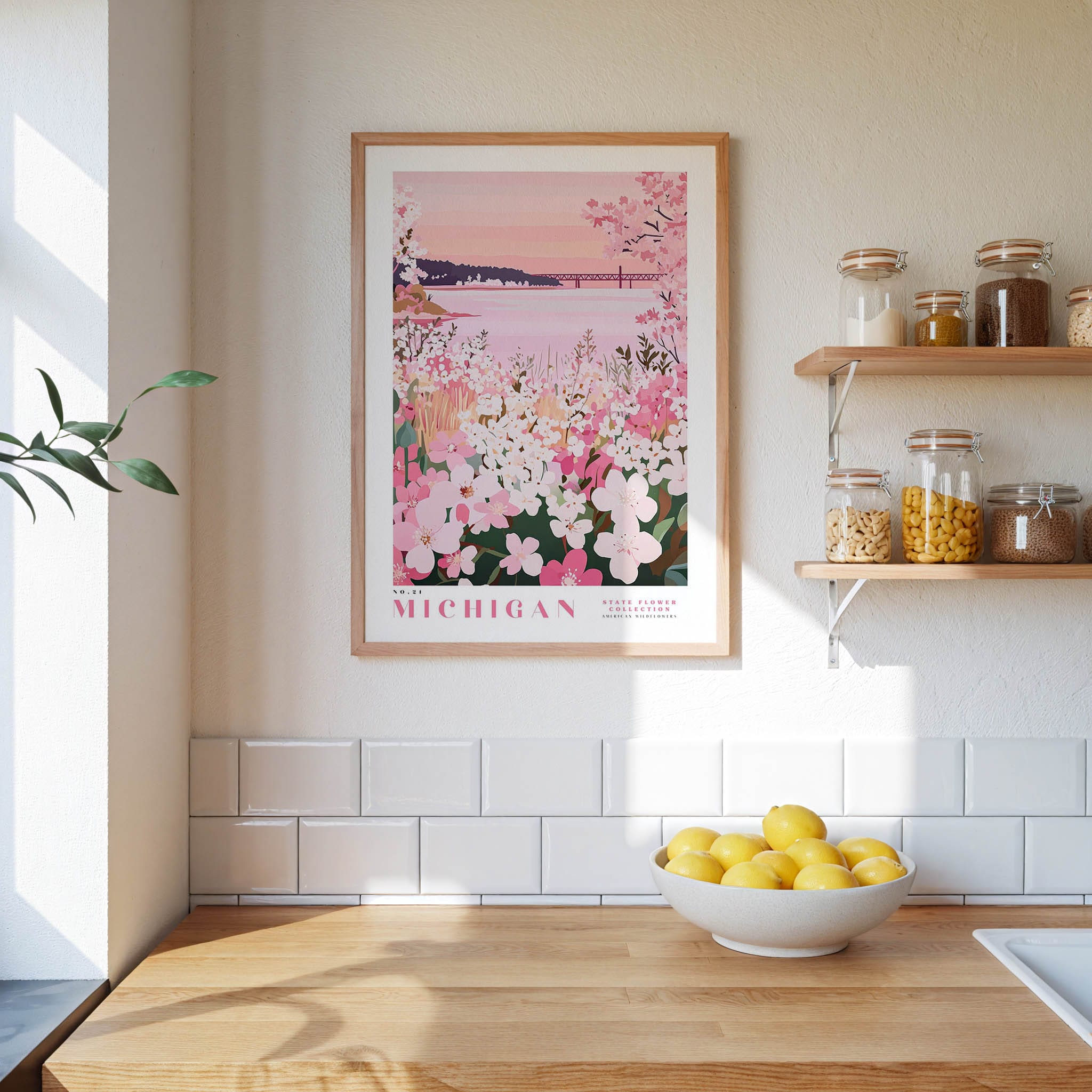 a kitchen scene with a framed poster of a flowery landscape hanging on the wall, a bowl of lemons on the counter, and shelves displaying various jars and containers.