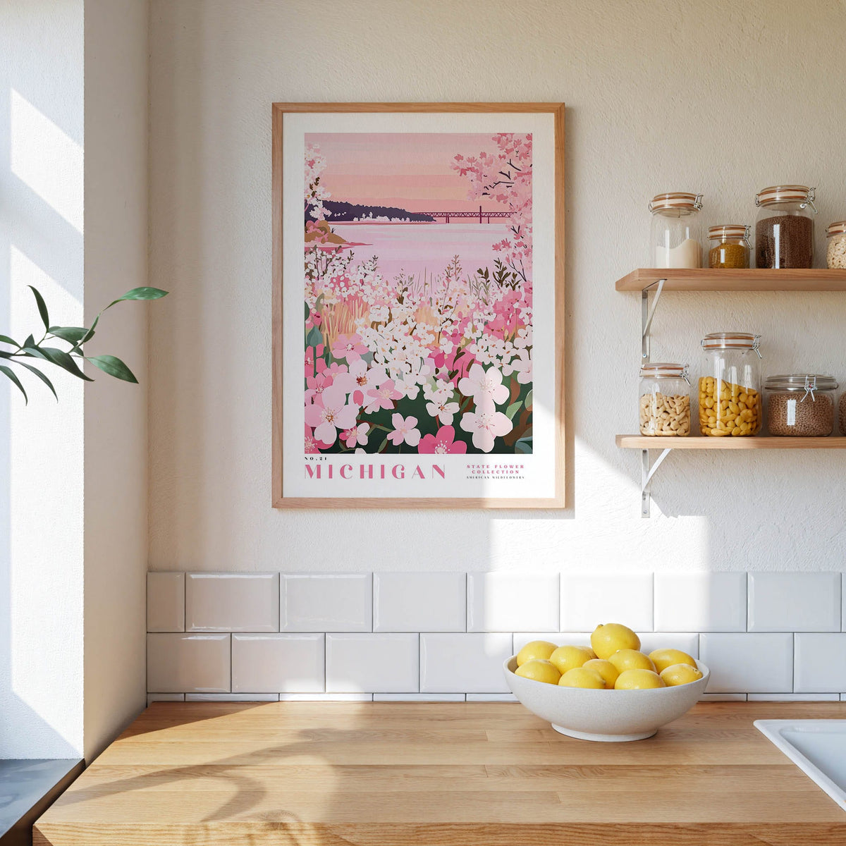 a kitchen scene with a framed poster of a flowery landscape hanging on the wall, a bowl of lemons on the counter, and shelves displaying various jars and containers.