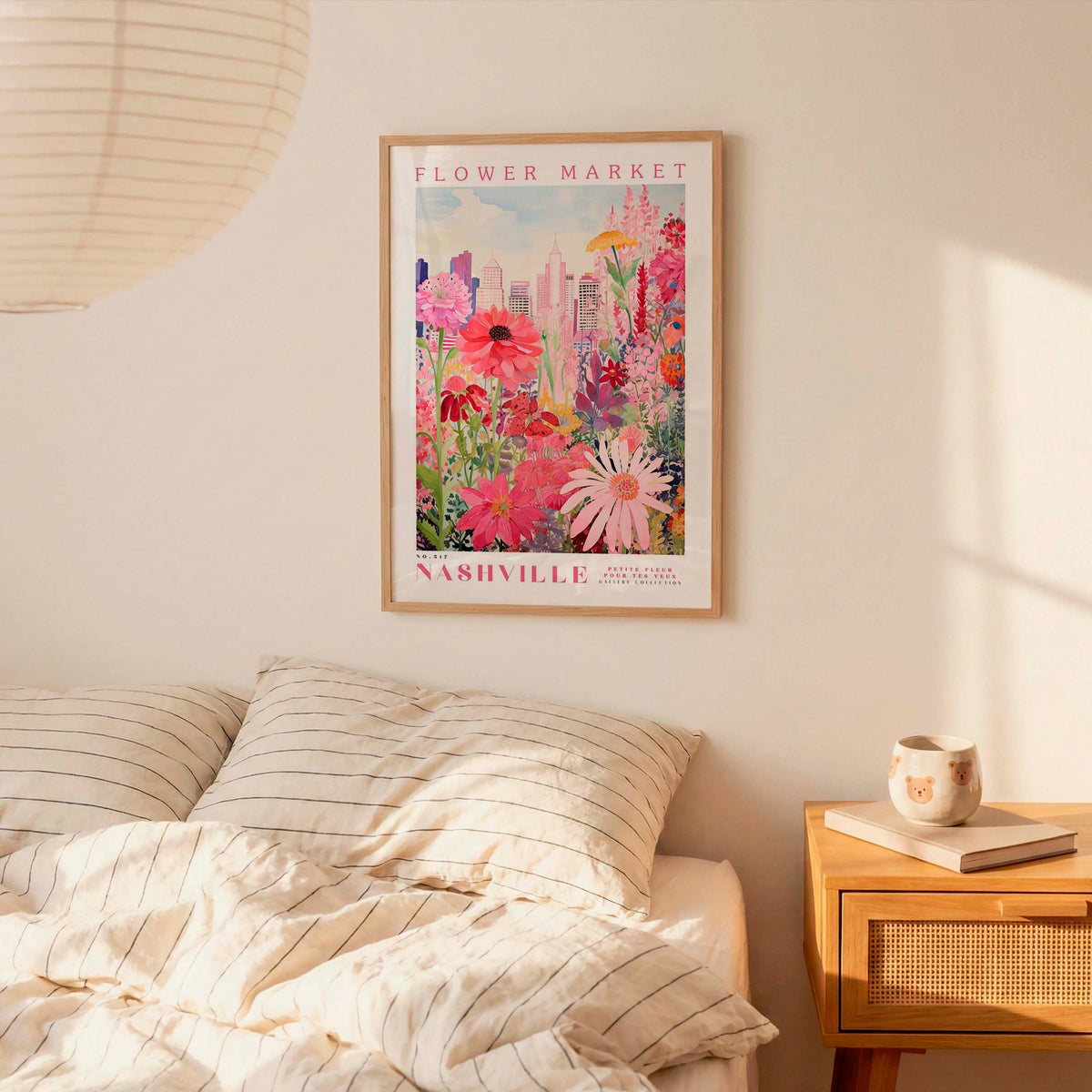 a bedroom scene with a framed poster of a colorful flower market in Nashville hanging on the wall above a bed with striped pillows.
