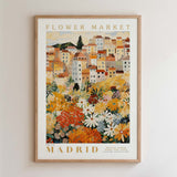 The image is a framed poster depicting a colorful and vibrant cityscape with a variety of flowers and plants in the foreground.