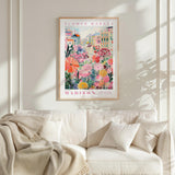 a framed poster of a colorful floral scene hanging on a wall above a white couch with a blanket draped over it.