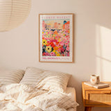 a bedroom setting with a framed poster of a colorful flower market hanging on the wall above a bed with striped pillows.