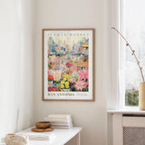 a framed poster of a colorful flower market in San Antonio, Texas, hanging on a wall.