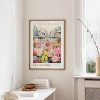 a framed poster of a colorful flower market in San Antonio, Texas, hanging on a wall.