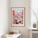 a framed poster of a colorful illustration of a flower market in New Orleans, with a cityscape in the background. The poster is hanging on a wall, and there is a small table with books and a vase nearby.