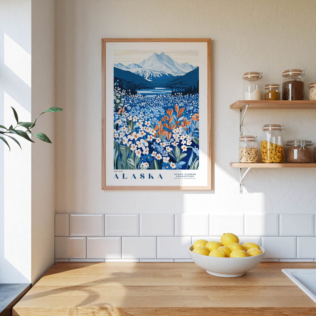 a framed poster of a scenic landscape with mountains and a field of flowers, hanging on a wall above a wooden counter with a bowl of lemons.