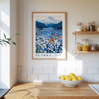 a framed poster of a scenic landscape with mountains and a field of flowers, hanging on a wall above a wooden counter with a bowl of lemons.