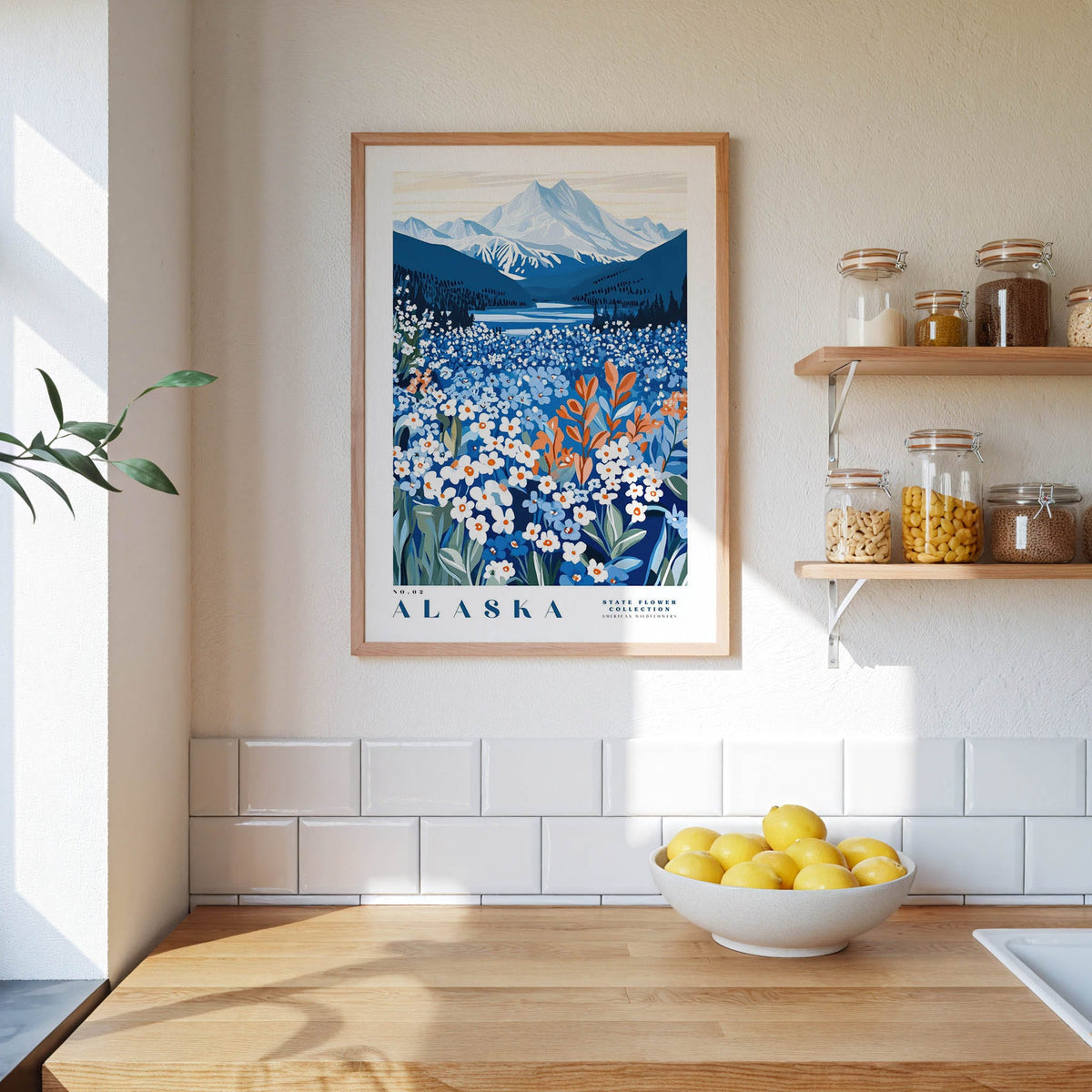 a framed poster of a scenic landscape with mountains and a field of flowers, hanging on a wall above a wooden counter with a bowl of lemons.